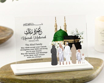 May include: A clear acrylic plaque with a white background featuring a calligraphic inscription in Arabic script that reads "Umrah Mubarak" and a depiction of the Kaaba in Mecca, Saudi Arabia. The plaque also includes a message of congratulations to the Afzal family on their Umrah pilgrimage.
