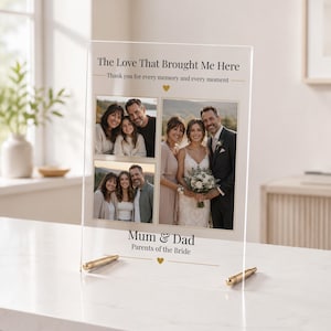 以下が含まれることがあります： 透明なアクリルのフォトスタンド。The Love That Brought Me Here、Thank you for every memory and every moment、Mum & Dad、Parents of the Brideという文字が印刷されています。家族と結婚式のカップルの写真が3枚収められています。