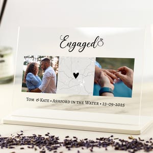 May include: Clear acrylic photo display with the word "Engaged" in script. The display features three photos, including a map with a heart, and the names "Tom & Kate" and the date "23-09-2025". The display sits on a white base.