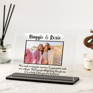 May include: A clear acrylic photo frame with a black base. The frame features a photo of two women smiling and making peace signs. The text "Maggie & Rosie" is at the top of the frame. The text "We've made so many fun memories, I can't wait to make more with you. Thank you for always being there for me. I'm so lucky to have you as a best friend." is at the bottom of the frame.