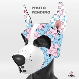 May include: A white dog muzzle with pink and blue ears. The ears are covered in a pattern of small, colourful icons. The muzzle is made of a soft, flexible material and has a comfortable fit.