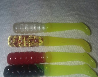 May include: Four different colored fishing lures with a yellow, green, and black color scheme. The lures are made of soft plastic and have a segmented body.