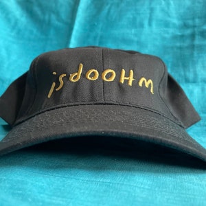May include: A black baseball cap with a gold embroidered inscription that reads "isdoOHM".