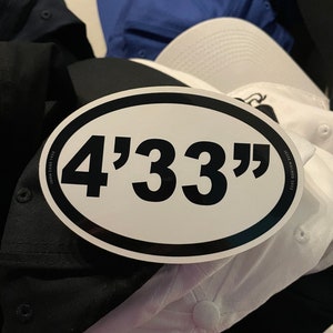 May include: A white oval sticker with a black border and the text "4'33" in black font.