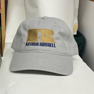 May include: A gray baseball cap with a gold embroidered "R" and the text "Arthur Russell" in navy blue.