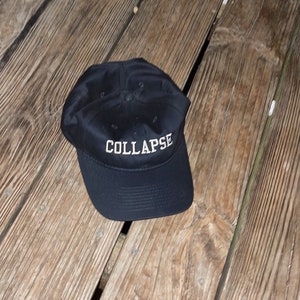 May include: A black baseball cap with the word "COLLAPSE" embroidered in white on the front.