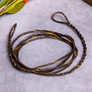 May include: A black and yellow braided bowstring for archery. The string is coiled up on a grey surface.