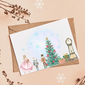 Könnte beinhalten: Eine Aquarell-Weihnachtskarte mit einem geschmückten Baum, einer Uhr und Figuren aus dem Ballett Der Nussknacker. Die Karte befindet sich auf einem braunen Umschlag, mit Schneeflocken und trockenen Zweigen im Hintergrund. Der Baum ist mit roten Kugeln geschmückt.