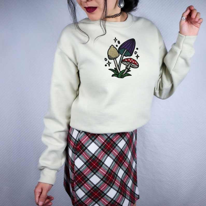 Magical mushroom cluster embroidery file in a fantasy fairy garden. Cute mushrooms from a magical garden. Shown on a tan crewneck sweater.