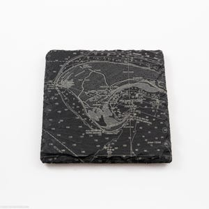 May include: A square, black slate coaster with a detailed nautical chart design. The chart features the Provincetown Harbor area, with text including "Provincetown Harbor" and depth measurements. The coaster has a textured surface and a natural, chiseled edge.