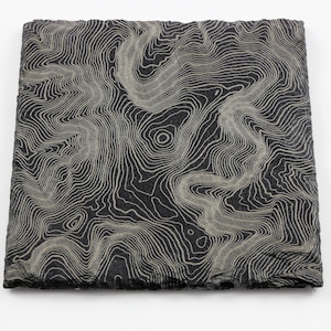 May include: Square, dark gray coaster with a topographic map design in light gray. The coaster has a rough, textured edge and a detailed pattern resembling contour lines. The design is centered on the coaster.
