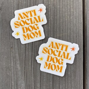 May include: Two white stickers with the text "Anti Social Dog Mom" in orange letters and a small yellow star on each sticker.