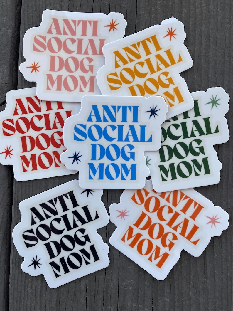 May include: A set of ten stickers with the text "Anti Social Dog Mom" in various colors and fonts. The stickers are on a wooden surface.