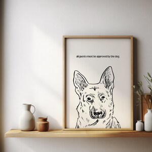 Könnte beinhalten: Eine Schwarzweißillustration eines Deutschen Schäferhundes mit dem Text "all guests must be approved by the dog" über dem Kopf des Hundes. Die Illustration ist in einem hellen Holzrahmen gerahmt und hängt an einer weißen Wand.