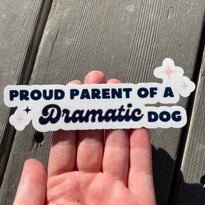 May include: White sticker with black text that reads "Proud Parent of a Dramatic Dog". The sticker has two small pink stars on either side of the text.
