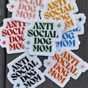 May include: Six white stickers with the text "Anti Social Dog Mom" in various colors and fonts. The stickers have a white background and are decorated with stars.