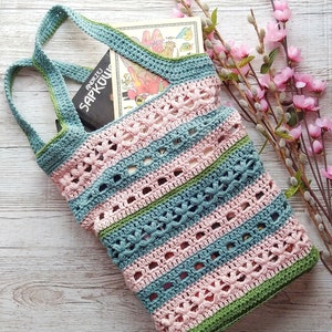 May include: A crocheted tote bag with green, blue, and pink stripes. The bag has a flower pattern and is filled with a book. The book has the title "Andrzej Sapkowski" on the cover.