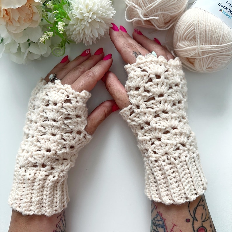 May include: A pair of crocheted fingerless gloves in a cream color. The gloves have a lacy pattern and are made with a soft yarn.