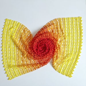 May include: A crocheted shawl with a gradient of yellow, orange, and red colors. The shawl is folded in a spiral shape, creating a flower-like design.
