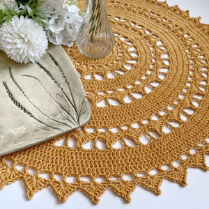 May include: A crocheted table runner in a warm yellow color with a delicate, intricate pattern. The runner is made with a fine yarn and has a scalloped edge.