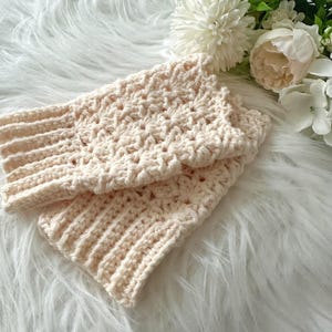 May include: A pair of crocheted fingerless gloves in a cream color. The gloves are made with a delicate stitch pattern and have a ribbed cuff.