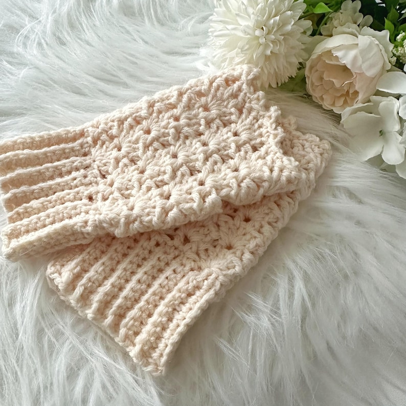 May include: A pair of crocheted fingerless gloves in a cream color. The gloves are made with a delicate stitch pattern and have a ribbed cuff.