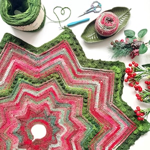 Peut inclure: Projet de crochet en forme d'étoile, fait à la main, dans les tons de rouge, vert et rose. L'image comprend du fil, un crochet, des ciseaux et des éléments décoratifs. La pièce finie a un trou au centre, suggérant un cache-pied de sapin.