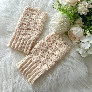 May include: A pair of crocheted fingerless gloves in a cream color. The gloves have a delicate, lacy pattern and are made with a soft yarn.