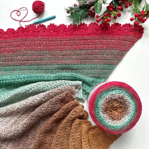 May include: A crocheted shawl in shades of brown, green, and red with a crocheted border. The shawl is folded and displayed with a ball of yarn in the same color scheme.