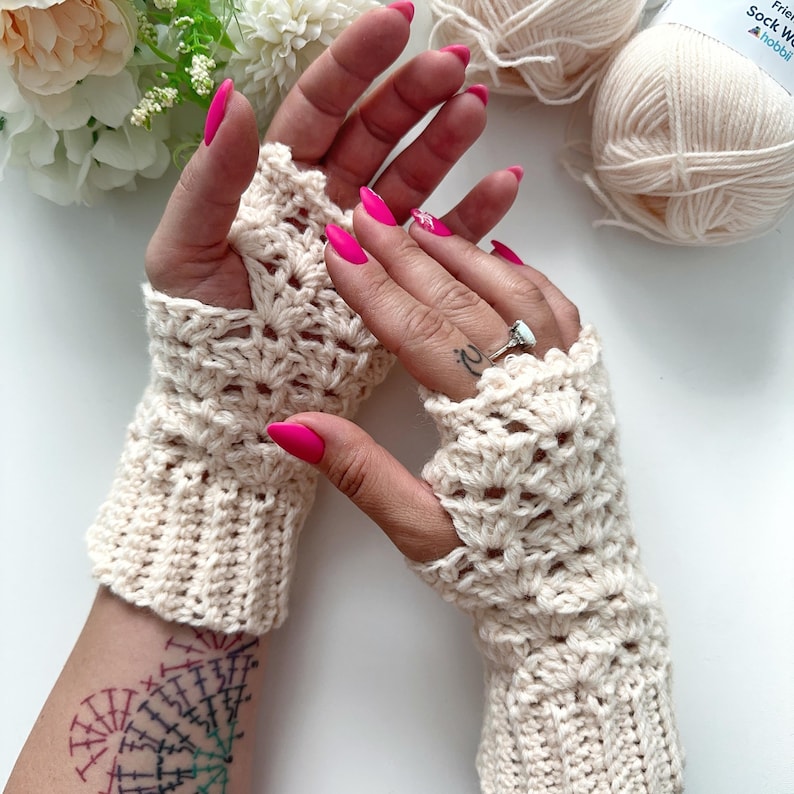 May include: A pair of crocheted fingerless gloves in a cream color with a lacy pattern. The gloves are shown on a person's hands with pink nail polish.