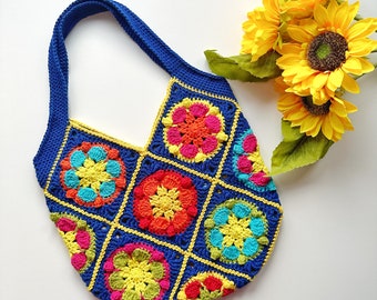May include: A crocheted tote bag with a blue background and colorful floral designs. The bag has a single strap and is made with a variety of bright colors, including yellow, orange, red, green, and blue.