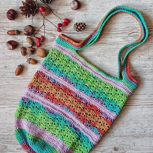 May include: A colorful crocheted tote bag with a striped pattern in shades of green, blue, orange, and purple. The bag has a single long strap and is made with a textured stitch.