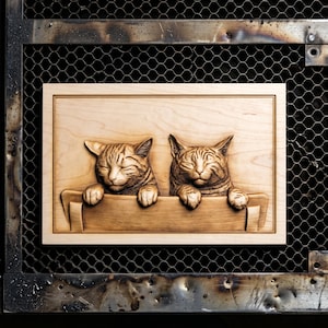 May include: Wooden relief carving featuring two tabby cats with closed eyes and paws resting on a ledge. The cats are smiling, and the carving is set within a rectangular frame. The wood has a light brown color.