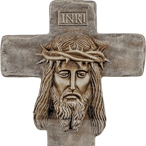 May include: A bronze-colored pendant in the shape of a cross with a detailed image of Jesus Christ's face. The cross has the inscription "INRI" on the top and bottom, which stands for "Jesus Nazarenus Rex Iudaeorum" or "Jesus of Nazareth, King of the Jews".