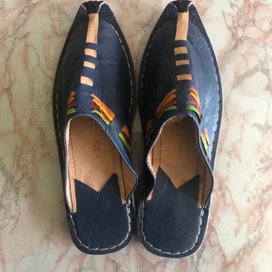 May include: A pair of blue leather slippers with colourful embroidery. The slippers have a pointed toe and a closed back.