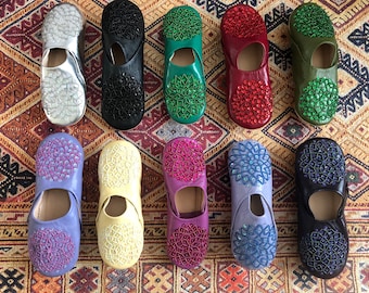 Puede incluir: Diez pares de zapatillas bordadas de colores con intrincados diseños florales. Las zapatillas son de cuero y tienen una variedad de colores, incluyendo morado, amarillo, rojo, verde y azul.