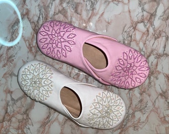 Puede incluir: Un par de zapatillas bordadas, una blanca con adornos plateados y otra rosa con adornos morados. Ambas zapatillas tienen un diseño floral.
