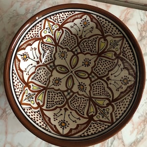 Può includere: Una ciotola in ceramica marrone con un motivo geometrico bianco e marrone. Il motivo presenta dettagli intricati e un design floreale.
