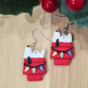 White dog on top of kennel with Christmas lights or holly made from polymer clay dangling from a sterling silver hook earing