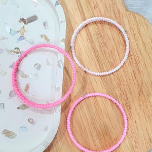 May include: Three beaded bracelets in pink and white. The bracelets are made of small, round beads and have a simple, elegant design.