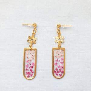 May include: Gold earrings featuring a dainty flower charm and a rectangular pendant filled with pressed pink and white flowers.