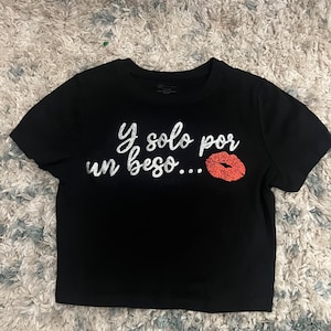 May include: Black cropped t-shirt with a silver glitter graphic that says "Y solo por un beso..." with a red glitter lip print.