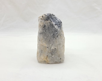 May include: A white crystal with black inclusions, a natural stone with a rough, irregular shape.
