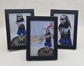 May include: Three framed art prints featuring a figure in a black shirt and blue shorts. The prints are in black frames. The central print has the text "Trailer Trash Tammy 2026" in gold script.