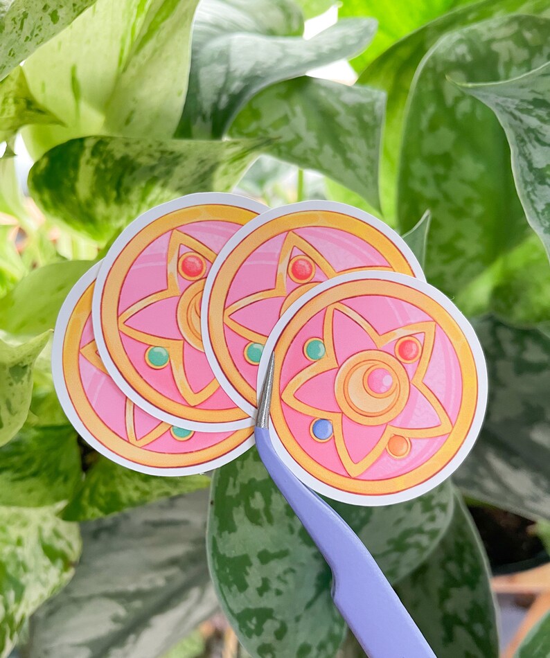 Peut inclure: Quatre autocollants roses et dor&eacute;s avec un motif d'&eacute;toile &agrave; cinq branches. L'&eacute;toile a un croissant de lune au centre et est entour&eacute;e d'un cercle de petites pierres pr&eacute;cieuses.