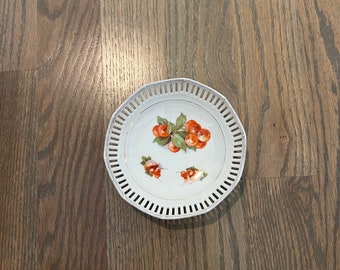 Peut inclure: Une assiette en céramique blanche avec un bord décoratif ajouré. L'assiette présente un motif peint à la main de cerises rouges sur une branche avec des feuilles vertes.