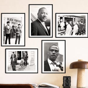 May include: A collection of framed black and white photographs featuring historical figures and scenes. The images include portraits and group shots, with one displaying the text "BLACK PANTHER PARTY". A desk with a lamp, camera, and open book is in the foreground.
