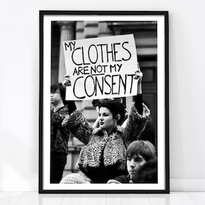 May include: Black and white framed print featuring a woman holding a sign that reads "MY CLOTHES ARE NOT MY CONSENT." The woman is wearing a patterned coat. Other people are in the background.