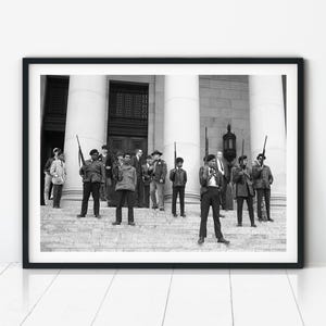 A black and white historic photograph of Black Panther Party members standing on the steps of the Washington State Capitol during a 1969 protest, holding firearms.