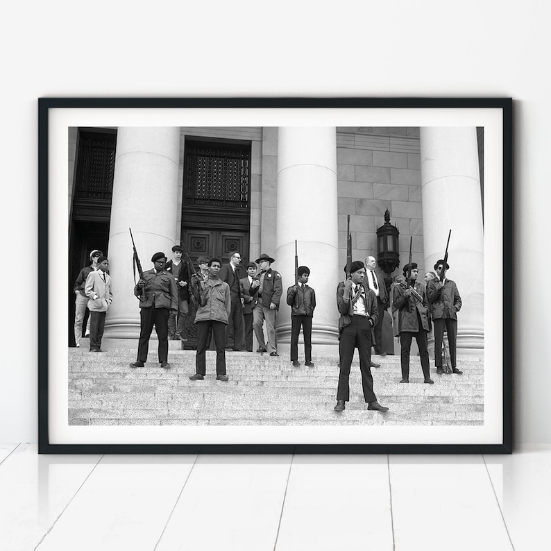 A black and white historic photograph of Black Panther Party members standing on the steps of the Washington State Capitol during a 1969 protest, holding firearms.